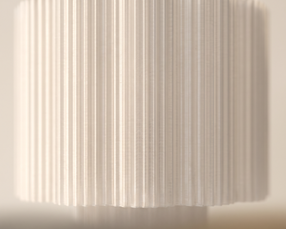 A close-up of a pleated fabric lampshade in a warm off-white or cream color, emitting a soft warm glow downward.