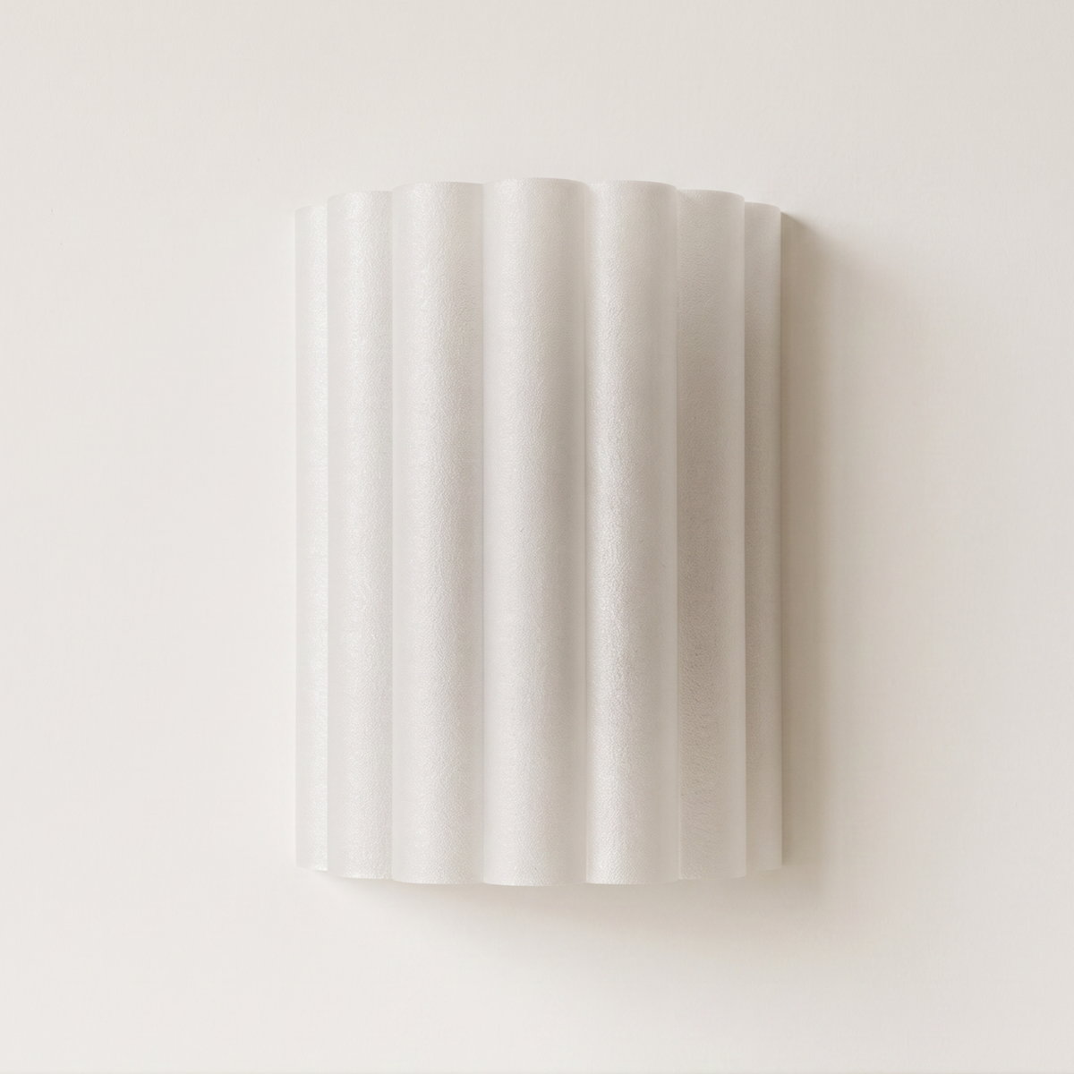 A modern wall-mounted sconce with a fluted, ribbed cylindrical shade in a warm off-white finish, shown against a minimalist beige wall and light stone ledge.